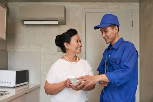 SmiIing technicial explaining Vietnamese senior woman how to use air conditioner remote control